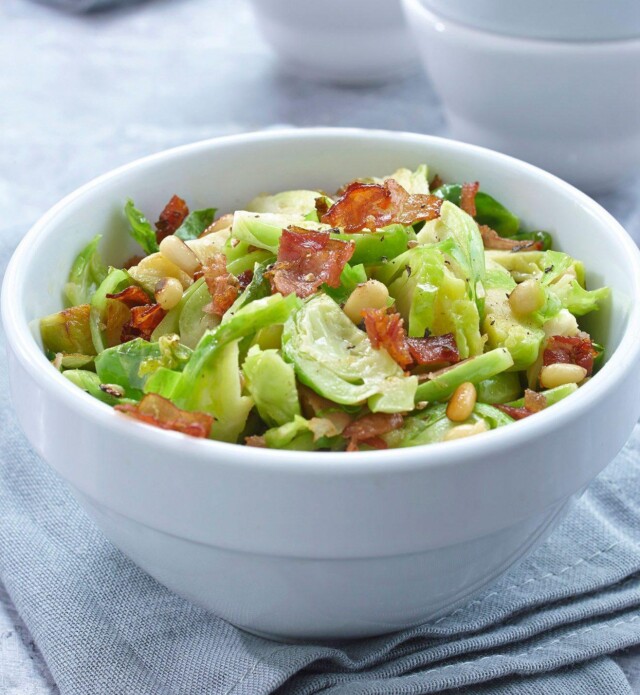 shredded brussle sprouts in a white bowl with prosciutto