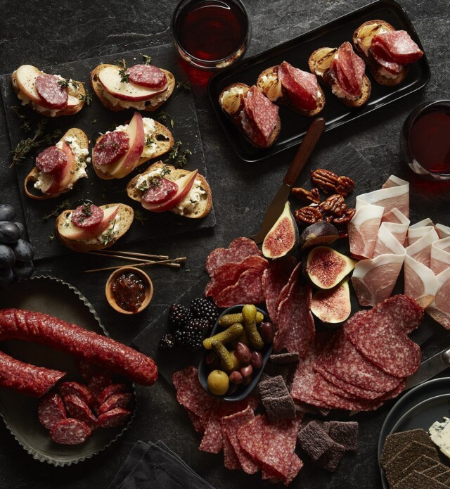 Charcuterie meats cheeses and fruit on a black slate