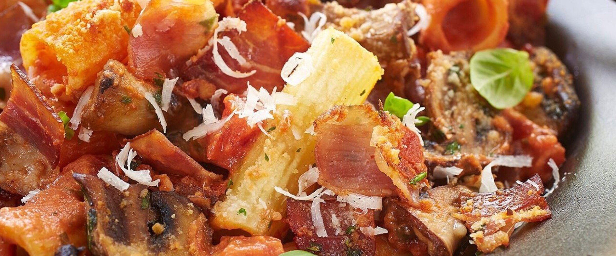 Baked rigatoni with speck prosciutto and parmesan cheese on a grey plate