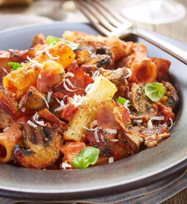 Baked rigatoni with speck prosciutto and parmesan cheese on a grey plate