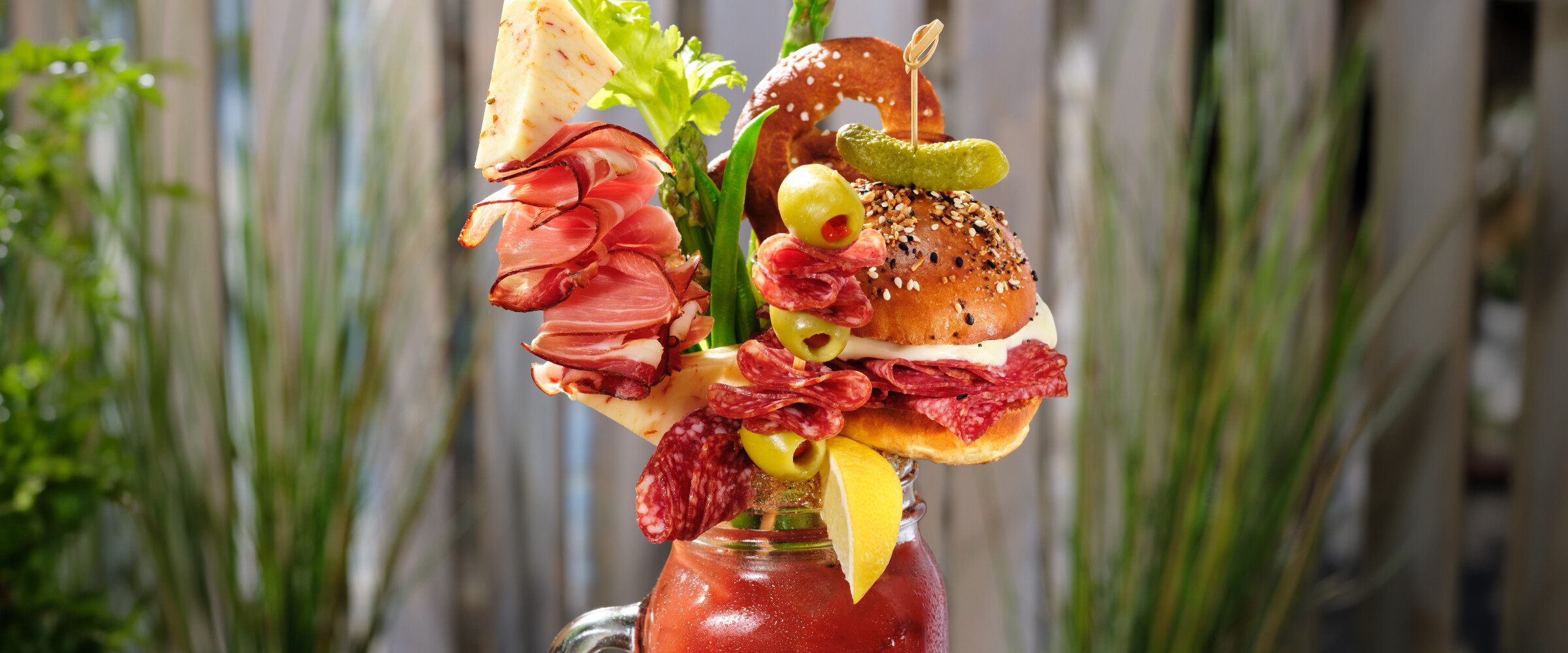 Bloody Mary drink on a table outside in a mason jar garnished with various meats and veggies.