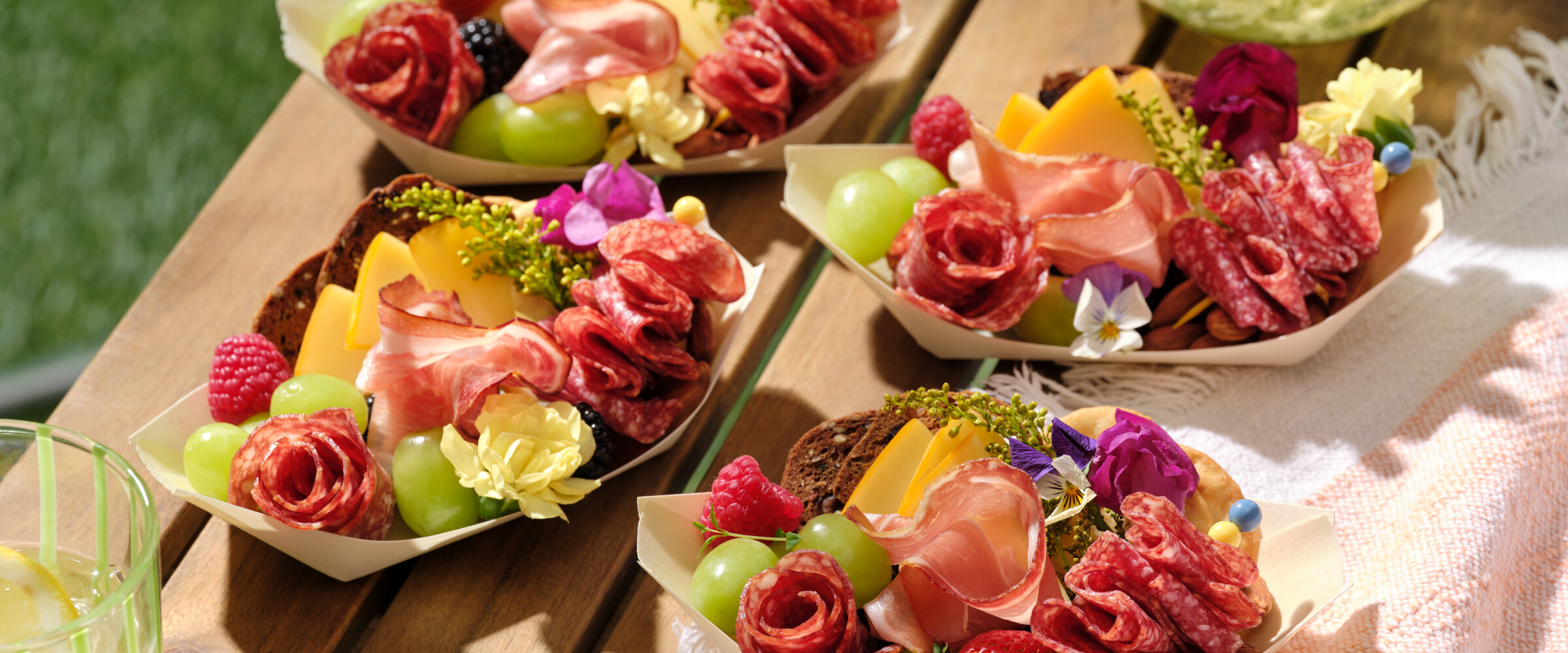 Charcuterie boats with various meats, fruits, and cheeses on an outdoor table.