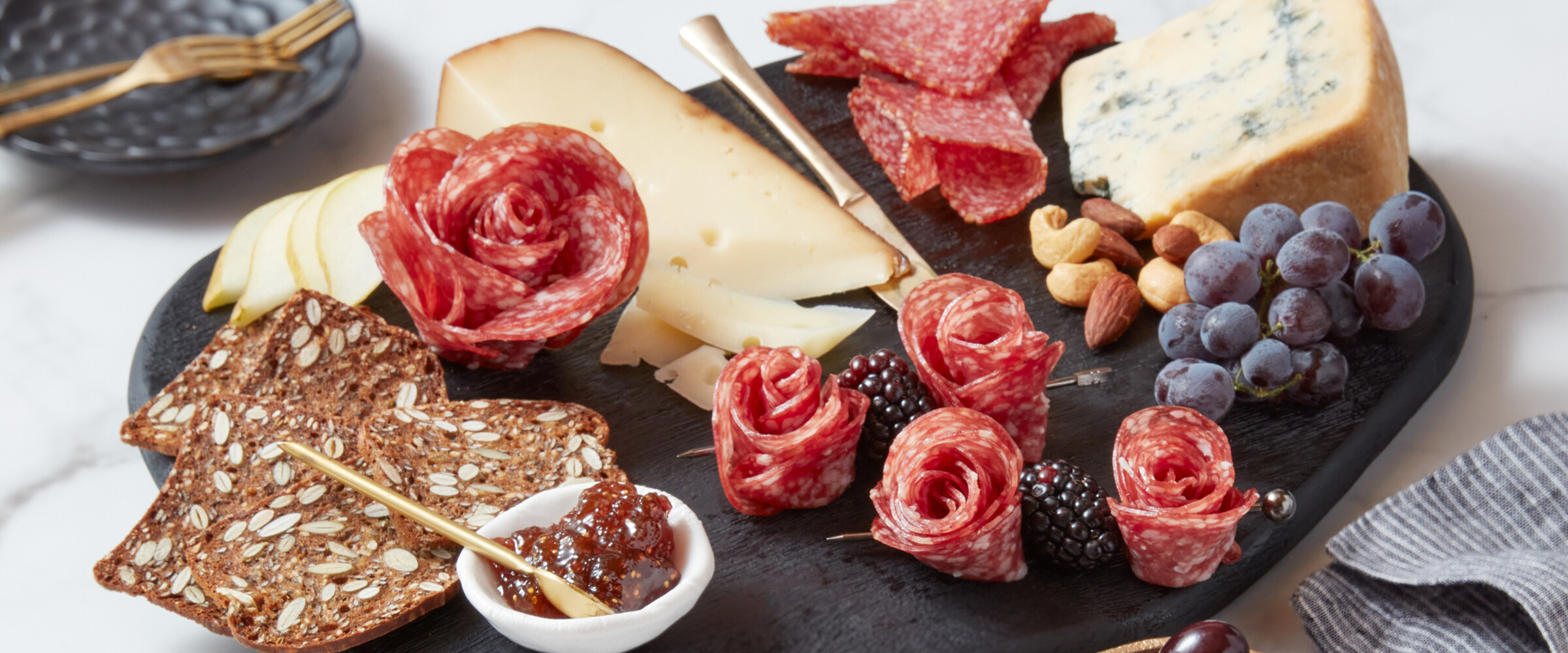 Salami roses on a board with crackers and cheese.