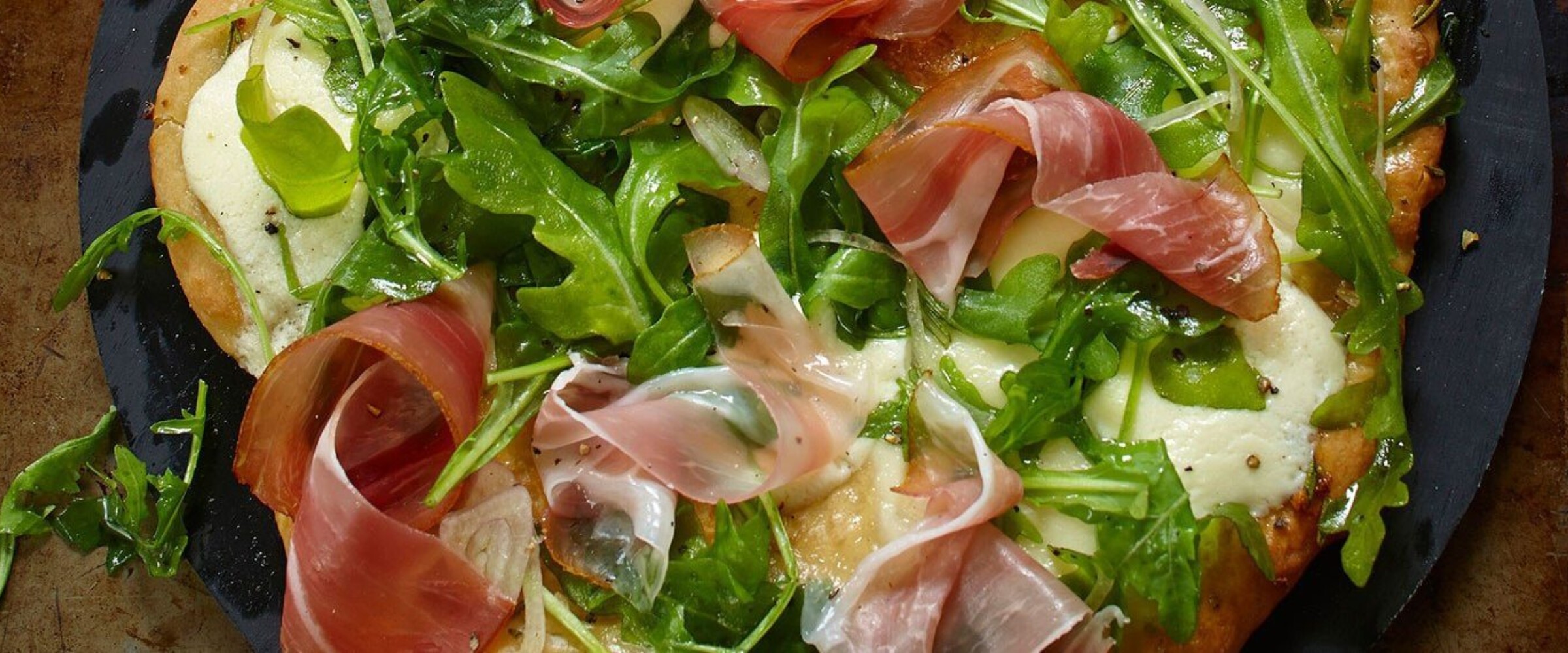 Arugula and prosciutto pizza on a black slate