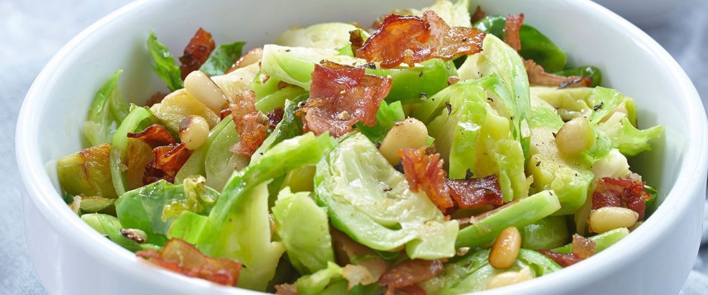 shredded brussle sprouts in a white bowl with prosciutto