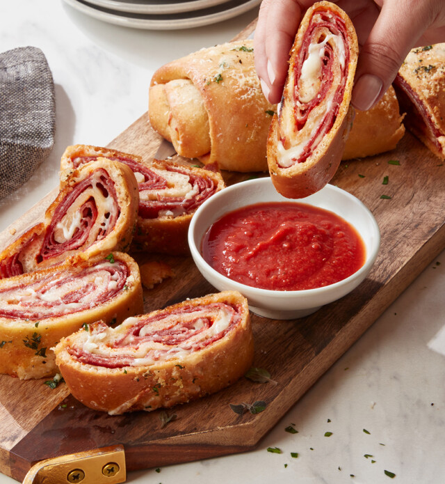 hand dipping stromboli into marinara sauce